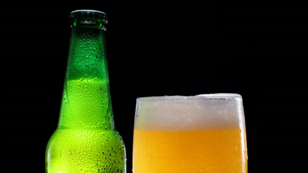Espuma de cerveza vertiendo en un vaso. Cerveza fría. botella de cerveza verde. — Vídeo de stock