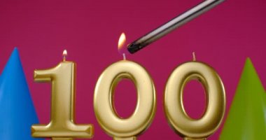 100 numaralı doğum günü pastası mumu yanıyor. Mutlu yıllar yıldönümü kutlaması konsepti. Arka planda doğum günü şapkası