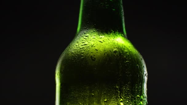 Nahaufnahme Rotation der grünen Bierflasche im Dunkeln. Kaltes Licht und erfrischendes Bier auf schwarzem Hintergrund. — Stockvideo
