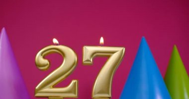 27 numaralı doğum günü pastası mumu yanıyor. Mutlu yıllar yıldönümü kutlaması konsepti. Arka planda doğum günü şapkası