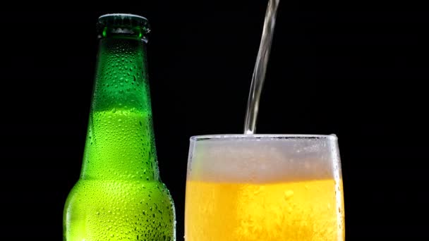 Giet pils en licht bier in een bierglas. Groene bierfles met waterdruppels. — Stockvideo