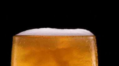 Siyah arka planda köpüklü ve köpüklü bardaklara hafif bira dökülüyor. Bira bardağında serinletici ve soğuk bira.