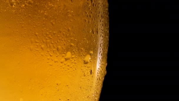 La cerveza fría ligera en el vaso con las gotas de agua rota. Taza de cerveza de cerca sobre un fondo negro. — Vídeos de Stock