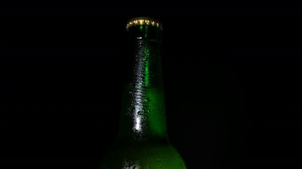 Kaltes Bier mit Wassertropfen auf Flasche wird von Licht aus der Dunkelheit beleuchtet — Stockvideo
