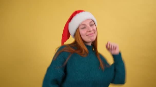 산타 크리스마스 모자를 쓴 빨간 스웨터를 입은 젊은 여성 이 노란 배경 스튜디오에서 손을 떼며 재미있는 몸짓을 하며 시간을 보내고 있습니다. 행복 한 새해 연휴 컨셉트 — 비디오