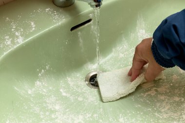 Adam lavaboyu temizleme pedi ve dezenfektan tozuyla temizliyor.