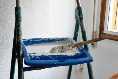 İçinde boya ve merdiven fırçası olan bir kap.