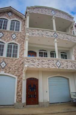 Gökyüzünde bulutlar, garnbde kapıları ve pencereleri olan büyük beyaz bir ev.