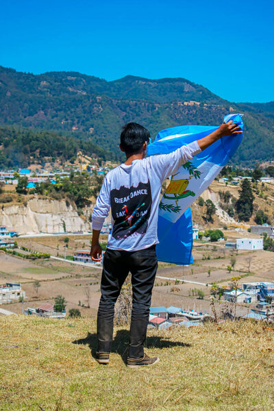 молодой человек с гватемальским флагом на скале с горами на заднем плане и дома