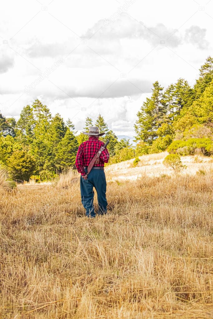man walking in dry grass with machete on his back