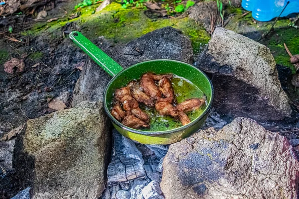 skillet with chicken wings cooked between rocks