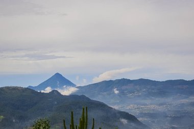 Gri gündoğumu bulutlarıyla mavi dağlar arasında volkan