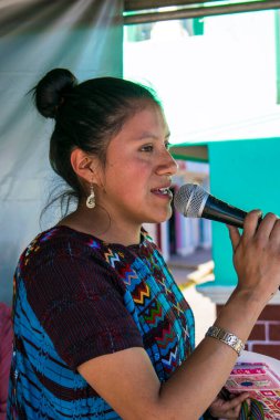 Kadın mikrofonla konuşuyor, tipik elbisesiyle