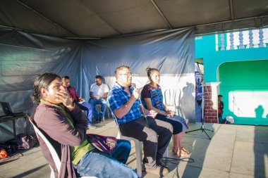 Gençler cajola festivalinde sahnede gri arka planda oturuyorlar