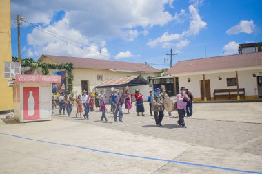 Maya yerlisi kadın ve erkek ellerinde çiçekler ve mavi gökyüzüyle sokakta yürüyorlar.