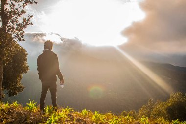 Siyah elbiseli genç adam ve beyaz bulutların arasından yükselen güneşin güzel gündoğumu.