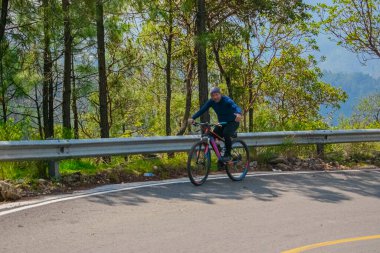 Bisikletli bir adam arka planda ağaçlarla yokuş yukarı gidiyor.