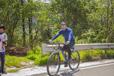 Siyah elbiseli, arka planda ağaçlı bisikletli bir adam.