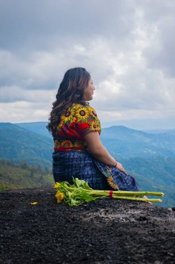 Güzel bir kadın, ayçiçeği çiçekleriyle oturuyor, beyaz bulutlar ve dağınık saçlar.