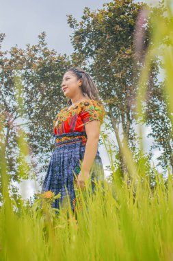 Arka planda ağaçlarla kuru çimlerin arasında dikilen kadın tipik Maya kostümü ile.