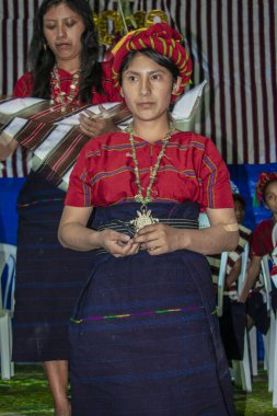 Kadın dizlerinin üstüne çöküp arka planda diğer kadınlar tarafından giydirilmiş.