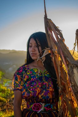 Profilde uzun siyah saçlı, bitki dallı bir kadın var.