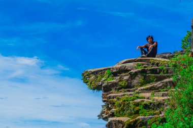 Genç adam mavi gökyüzü ile büyük kayaya baktı.