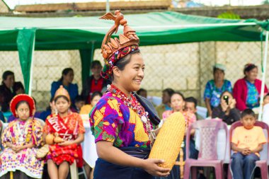 Güzel bir kadın elinde büyük mısırla halk içinde dans ediyor.