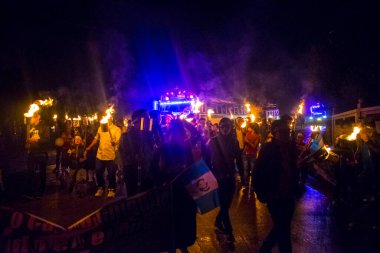 Arka planda meşaleler ve otobüslerle çalışan insanlar