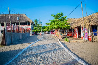 Yeşil ağaçlı taş yol ve çiftlikli mavi gökyüzü.