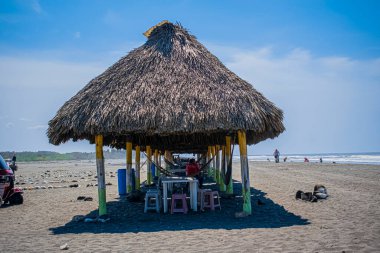 Masaları olan bir çiftlik ve kumsalda oturan insanlar.