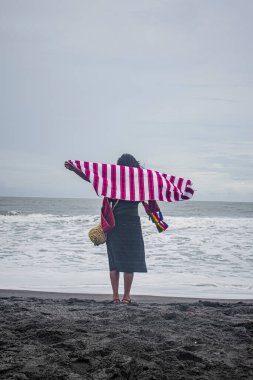 Sırtında duran Maya yerlisi kadın sahilde ve denizde duruyor.