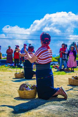 Kadın sepetiyle diz çöküp arka planda insanlarla dans ediyor.