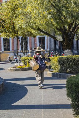 Yaşlı adam sırtında geleneksel davullar taşıyor.