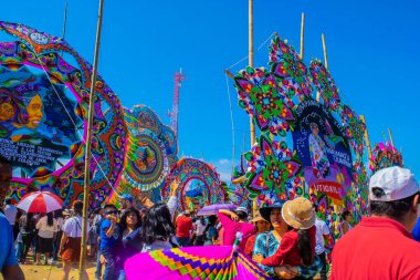 İnsanlar renkli uçurtmaları ziyaret ediyor. Üzerlerinde yazılı mesajlar olan figürler var.