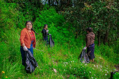 Siyah çöp torbalarıyla ormandan toplayan Maya yerlisi kadınlar.