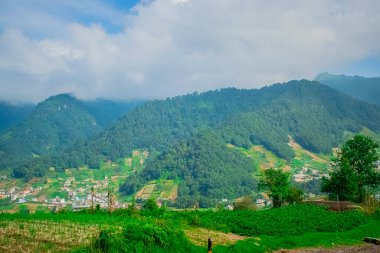 Altında bulutlar ve evler olan dağların manzarası