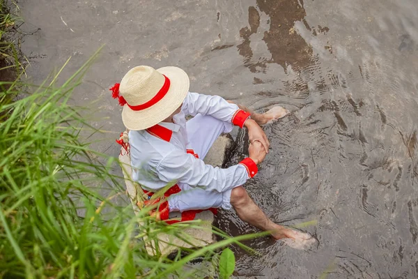 Maya yerlisi bir adam tipik kıyafetlerle nehirde oturuyor.