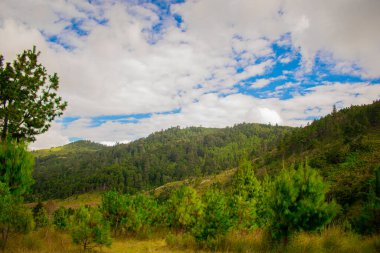 Mavi gökyüzünde yeşil dağlarla şekillenmiş bulutlar.