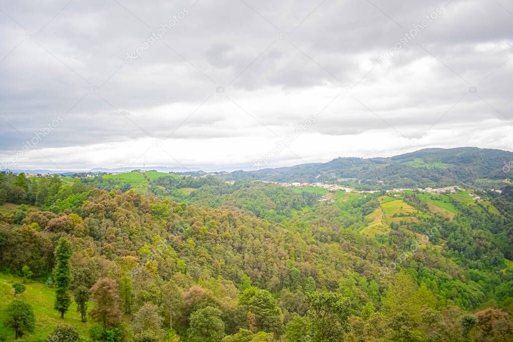 nice big green mountains surrounded by trees planted on the ground with cloudy sky