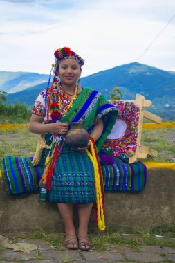 Genç bayan gülümsüyor, önünde güzel kumaşlar ve arkasında güzel bir manzara var.