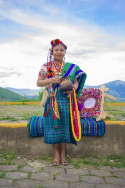 Genç bayan elinde kilden bir sürahi tutuyor. Arkasından güzel bir manzarası var.