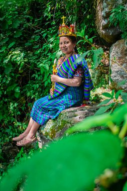 Maya prensesi doğanın etrafındaki bir kayanın kıyısında oturuyor.