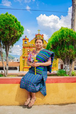 Genç bayan kilisenin önündeki bankta oturuyor, güzel yeşil ağaçların ve mavi gökyüzünün etrafında.