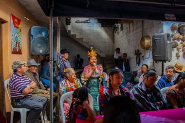 Mayalı kadın elinde mikrofonla konuşuyor, etrafındaki insanlar onu dinliyor.