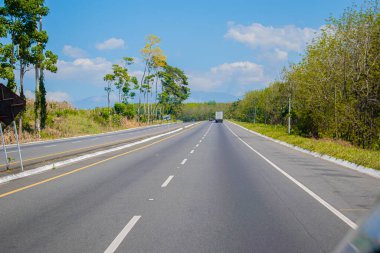 Arka planda güzel bir manzarayla caddeden geçen ağır bir nakliye aracı var.
