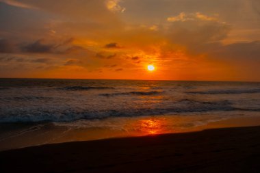 Beautiful sunset reddish sky, flared clouds waves, sea and sand