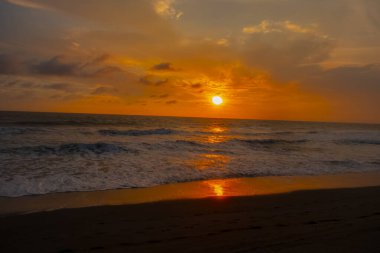 Beautiful sunset reddish sky, flared clouds waves, sea and sand