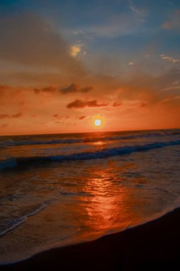 Beautiful sunset reddish sky, flared clouds waves in sea