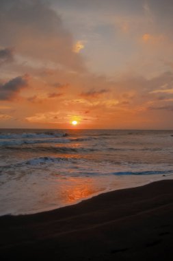 Beautiful sunset with waves in the sea and sand red sky flared with clouds.